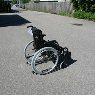 En kørestol uden ejermand. Den står udenfor på asfalten.